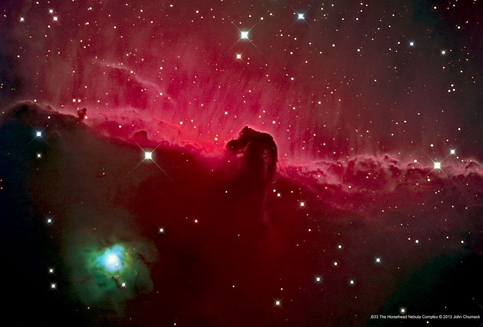 Vor einer roten Nebelwand über einem dunklen Horizont zeichnet sich eine pferdekopfähnliche dunkle Wolke ab. Links unten leuchtet ein Stern mit grüner Umgebung.