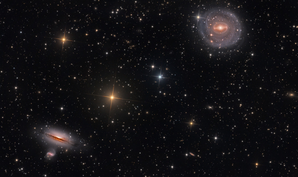 Links unten und rechts oben sind zwei markante Galaxien, die linke untere ist von der Seite zu sehen, darunter ist eine kleinere Galaxie. Die Galaxie rechts oben sehen wir von oben.