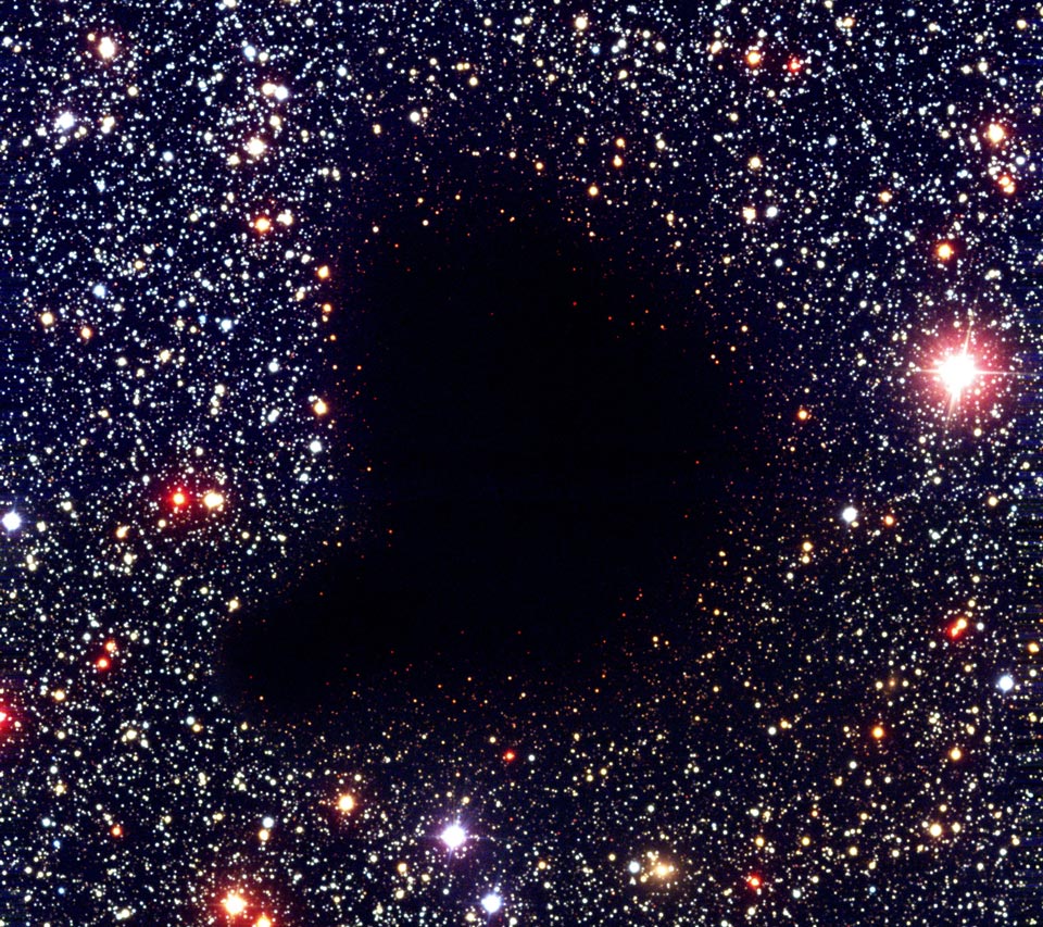 Mitten in einem sterngefüllten Bildfeld ist ein dunkler Fleck, es ist eine Molekülwolke, die die Sterne dahinter versteckt.