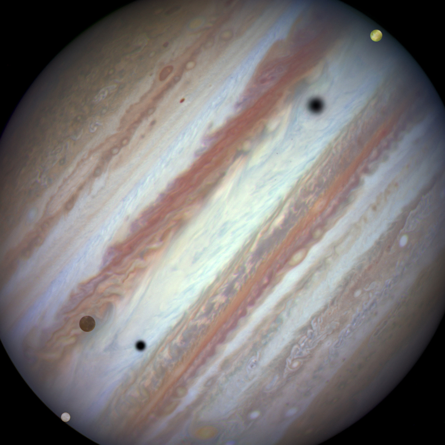 Vor dem Planeten Jupiter schweben drei der vier galileischen Monde: Io, Europa und Kallisto. Auch die kleinen Monde Thebe und Amalthea sind im Bild.