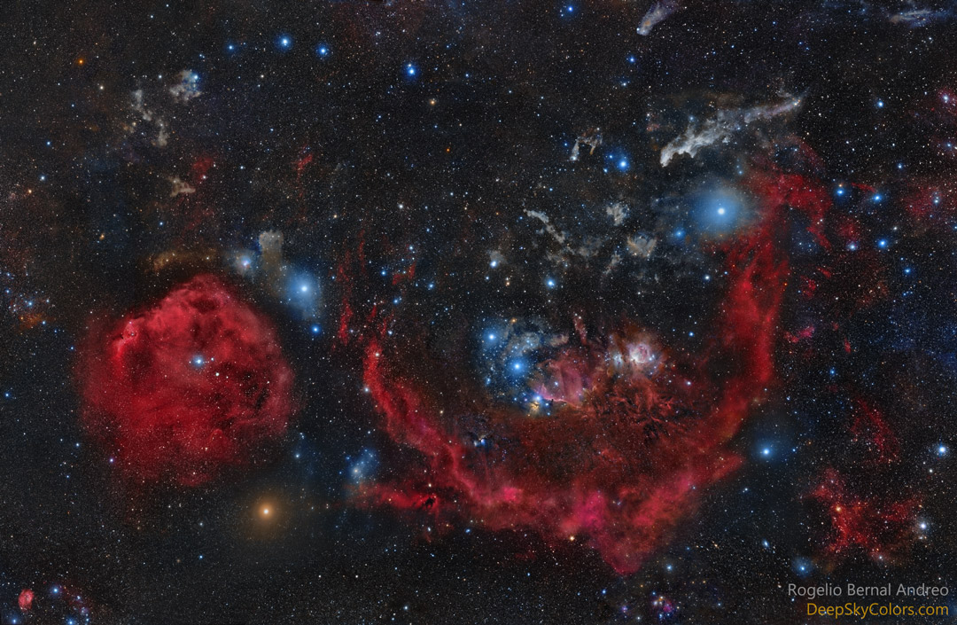 Im Bild liegt das berühmte Sternbild Orion, links ist der Kopf, der Bogen ist nach oben gerichtet. Oben ist ein runder roter Nebel, rechts die halbkreisförmige rote Barnardschleife, in der Mitte schräg übereinander die blau leuchtenden Gürtelsterne.