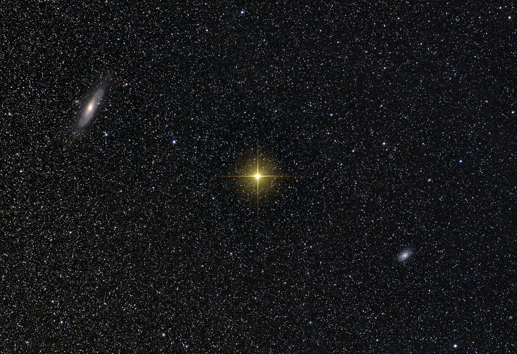 In der Mitte leuchtet der gelbliche, gezackte Stern Mirach, links darüber und rechts darunter sind kleine Galaxien, die drei Objekte bilden eine Diagonale im Bild.