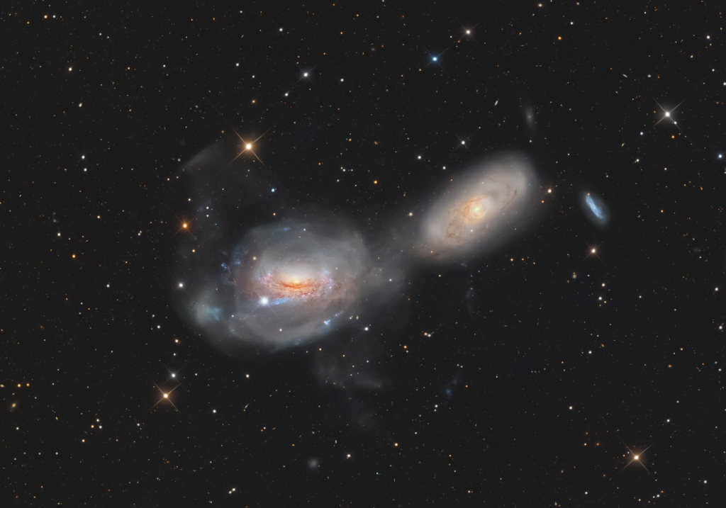 Mitten im Bild leuchten zwei verschwommen wirkende große Galaxien. Sie erinnern an zwei Augen.