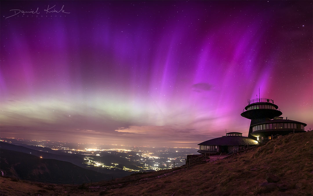 Der Himmel beim Tadeusz-Hołdys-Observatorium auf der Schneekoppe im Riesengebirge ist in purpurfarbene Polarlichter getaucht. Dahinter liegen die Lichter von Städten.