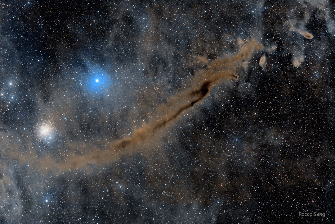 Der dunkle Dingsbums-Nebel (Dark Doodad Nebula) verläuft diagonal von links unten aufwärts durchs Bild. Links darüber sind der Kugelsternhaufen NGC 4372 und der blau leuchtende Stern Gamma Muscae im Sternbild Fliege.