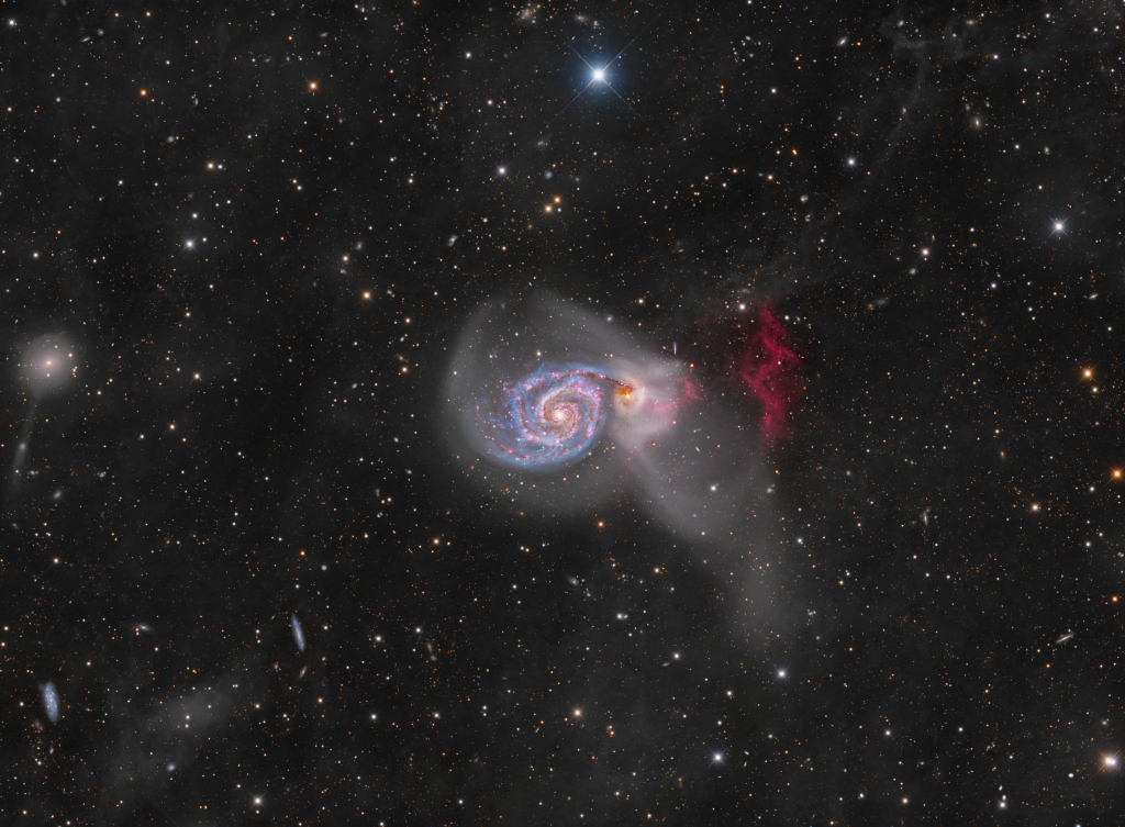 Die Galaxie M51 mit ihrer Begleiterin ist auf diesem Bild von diffusen Hüllen umgeben, rechts leuchtet eine rot leuchtende Wasserstoffklippe.