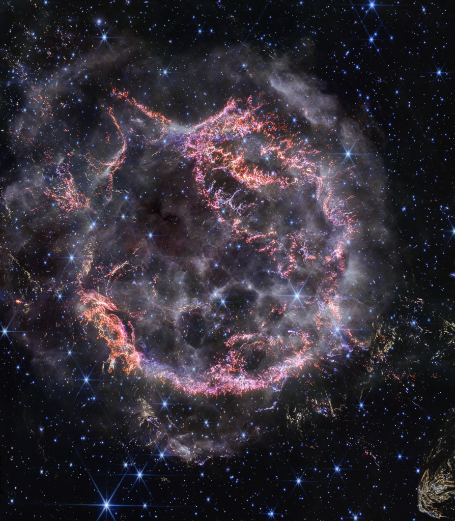 Vor einem dunklen Sternenhimmel mit vielen bläulich leuchtenden Sternen ist eine ringförmige Wolke zu erkennen. Einige Bereiche sind rötlich und knotig, andere sind weißlich und rauchähnlich.