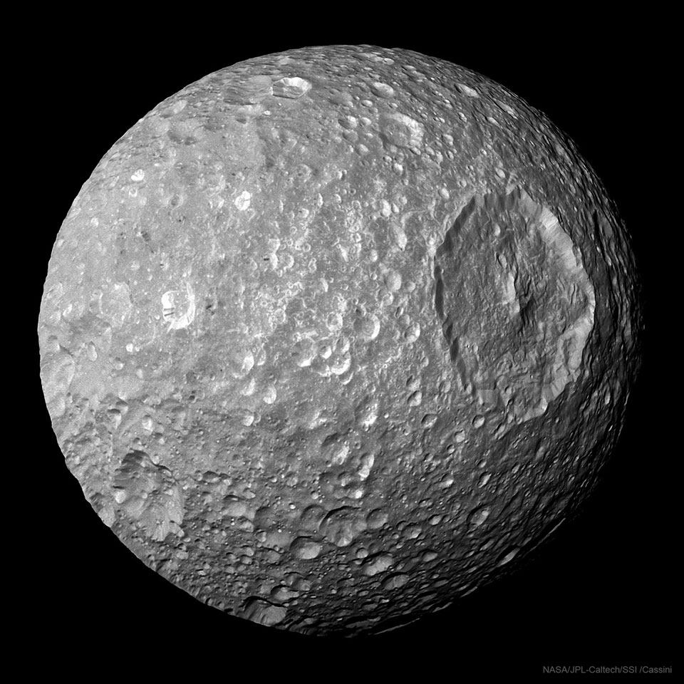 Der kleine Saturnmond Mimas besitzt einen riesigen Krater. Auf älteren Bildern erinnert er an den Todesstern aus Star Wars. Im Bild ist der Krater rechts oben, der Zentralberg zeichnet sich markant ab.