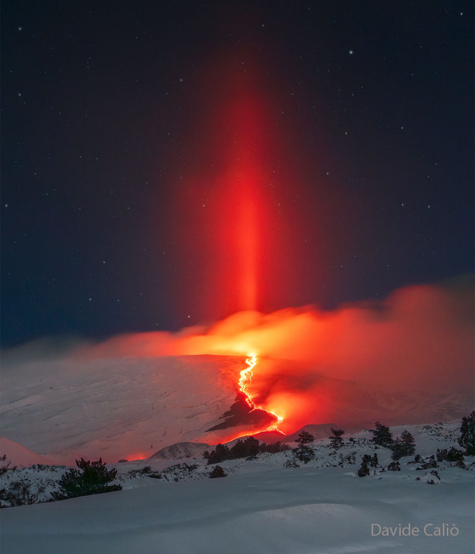 Lava fließt über eine eisige Landschaft, links steigt Nebel auf. Über der Lava ragt eine rote Lichtsäule auf, wo sich das Licht der Lava an Eiskristallen spiegelt.