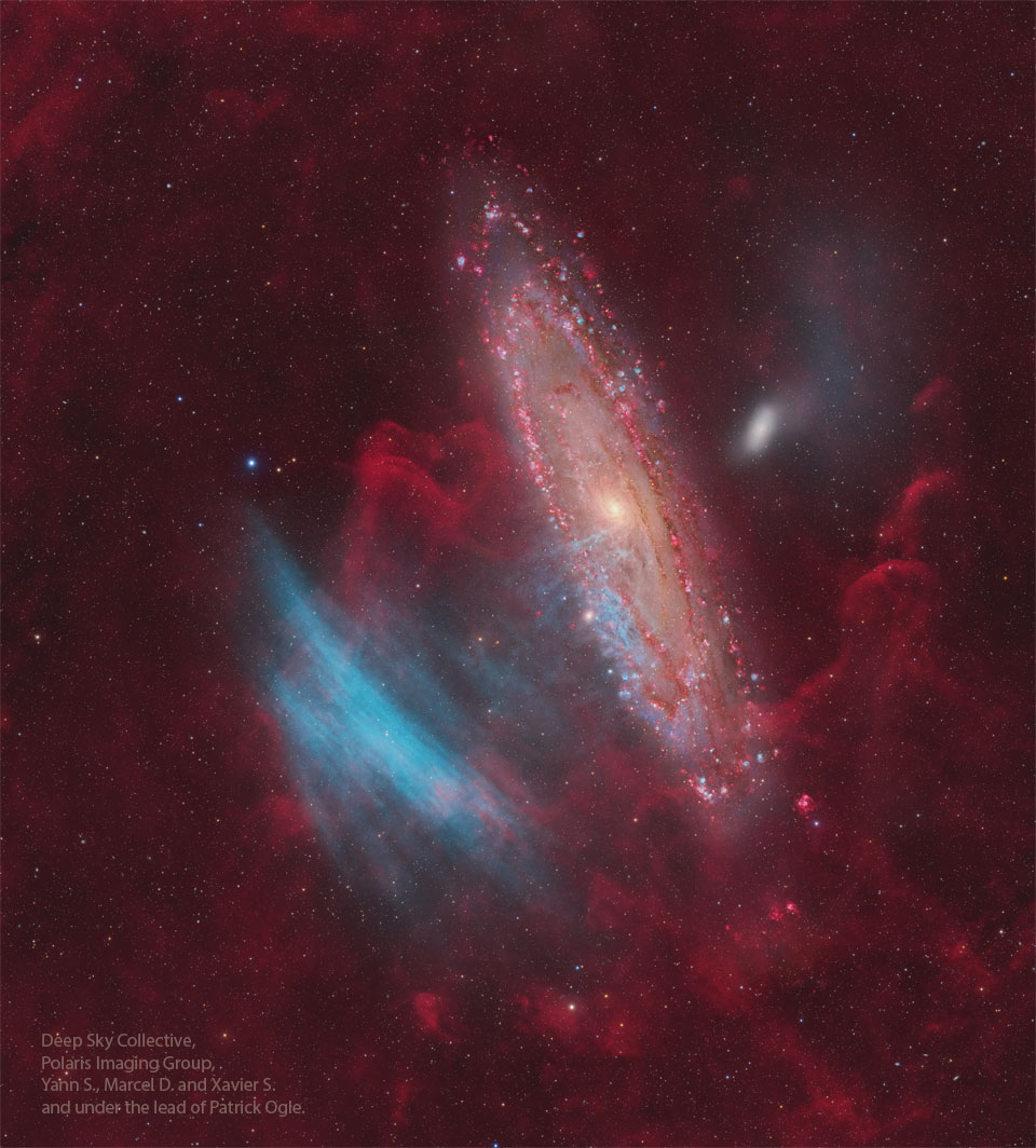 Die Andromedagalaxie liegt steil im Bild. Ihre Spiralarme sind rot gesprenkelt. Links daneben leuchten blaue Nebel. Außerdem ist die Galaxie von rötlichen Wolken umgeben.