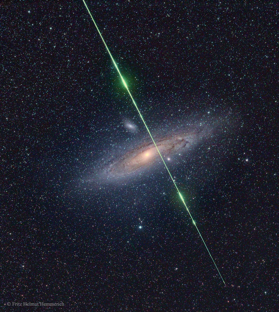 Ein Meteor blitzt vor der fernen Andromedagalaxie Messier 31 auf. Die lange Spur lodert immer wieder grünlich auf. Sie trifft fast das Zentrum von M31.