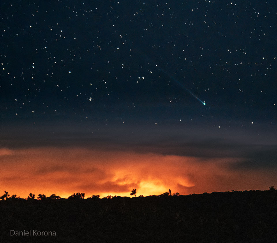 Über dem Horizont, der feuerrot leuchtet, breitet der Komet C/2025 R2 (SWAN) seinen Schweif am Sternenhimmel aus.