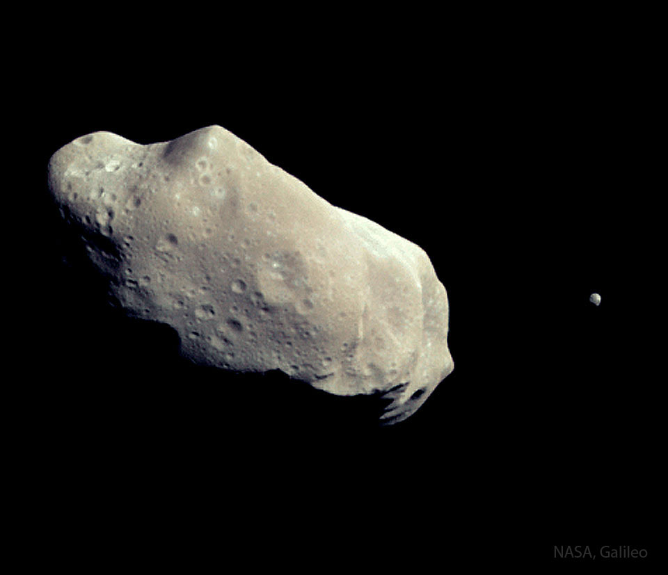 Links ist ein unregelmäßiger, kartoffelförmiger Körper, rechts daneben ein winziger kleiner Körper. Es sind der Asteroid Ida mit seinem kleinen Mond Dactyl.