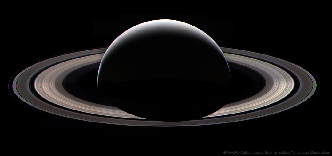 Wir sehen auf die Nachtseite von Saturn. Oben ist der Planet sichelförmig von der Sonne beleuchtet. Sein Schatten fällt auf die Ringe, die ebenfalls im Sonnenlicht liegen. Die Cassini-Teilung ist eine markante dunkle Lücke in den Ringen.