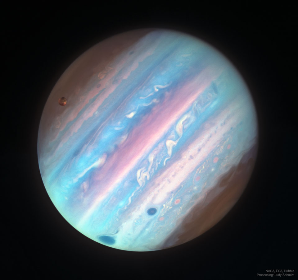 Jupiter, der fast das Bild füllt, wirkt hier seltsam. Er wurde hier in UV-Licht abgebildet, die Aufnahme wurde mit Falschfarben gefärbt. Daher ist der Rote Fleck dunkelblau. Links oben ist Jupiters großer Mond Ganymed.