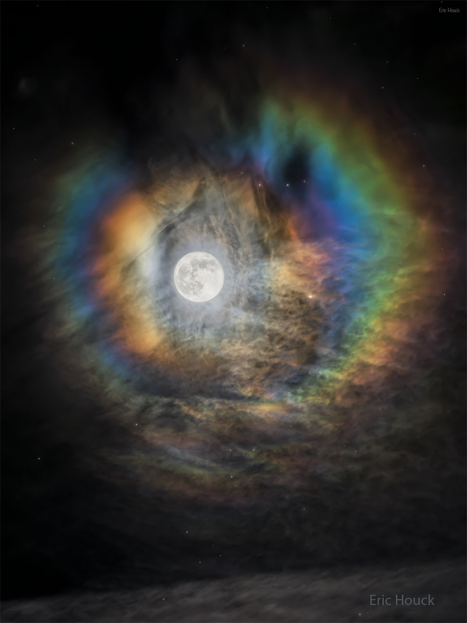 Der volle Mond leuchtet durch dünne Wolken, deren wellige Struktur sichtbar ist. Der Mond ist umgeben von konzentrischen farbigen Ringen, die einem kreisrunden Regenbogen ähneln.