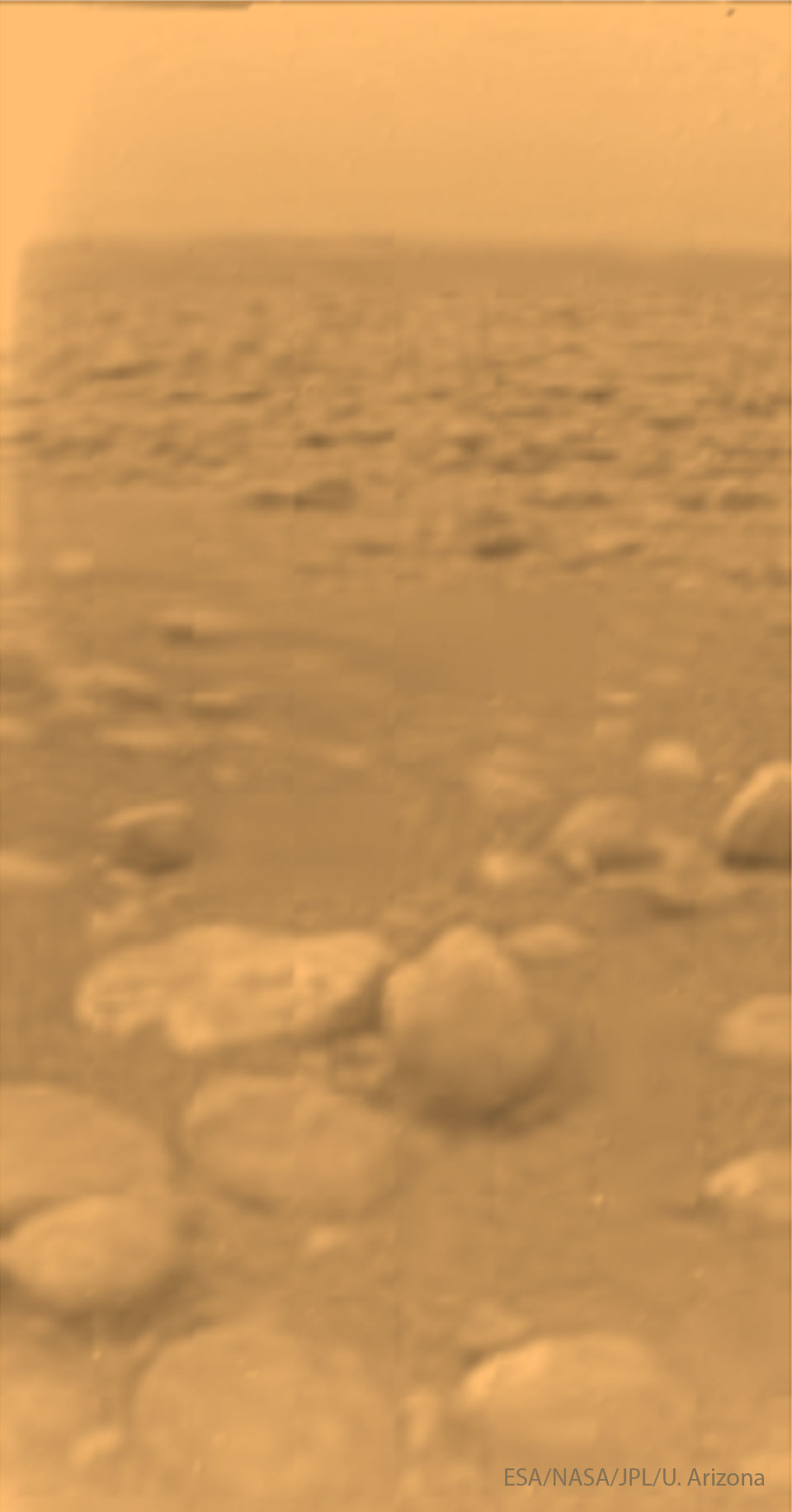 Das verschwommene Bild zeigt eine steinige Landschaft, die in orangefarbenes Licht getaucht ist. Die sensationelle Aufnahme stammt von der Landesonde Huygens, die mit Cassini zu Saturn flog und auf dem Mond Titan landete.