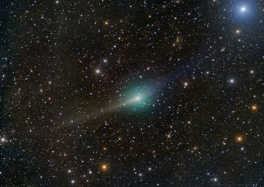 Von vielen kleinen Sternen umgeben zieht der interstellare Komet 3I/ATLAS durchs Bild. In der Mitte ist seine grünliche Koma, nach links zeigt ein gelblicher Staubschweif, und der bläuliche Ionenschweif breitet sich nach links aus. Rechts oben ist ein heller blauer Stern.