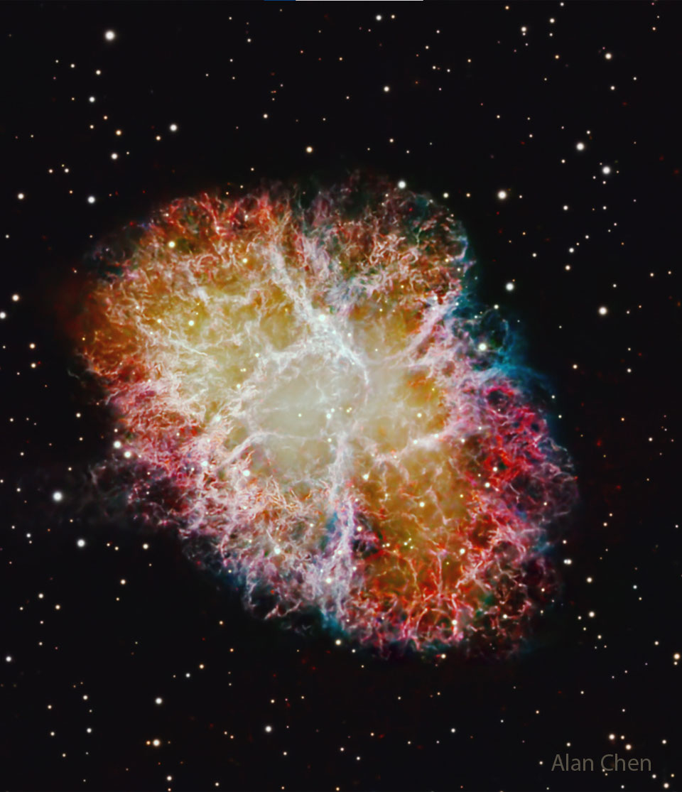 Vor einem schwarzen, sternenbesetzten Hintergrund steht eine ovale Wolke mit faseriger Struktur. DIe Fasern leuchten weiß, rot und blau und der Kernbereich der Wolke leuchtet diffus gelblich.