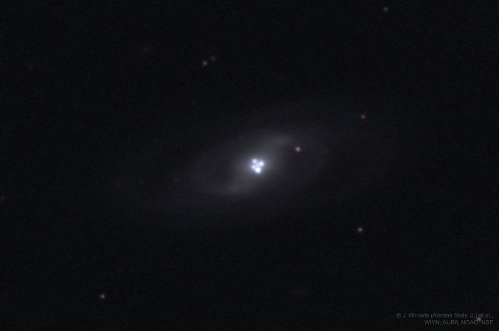 Die sehr blasse Galaxie im Bild hat scheinbar vier sehr helle Kerne. Diese gehören jedoch nicht zur Galaxie, sondern sind das Licht eines Quasars, der weit dahinter liegt. Das Objekt ist als Einsteinkreuz bekannt.
