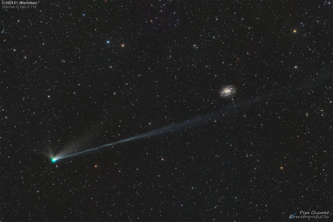 Links unten ist der blaugrüne Kopf des Kometen Wierzchoś. Seine Schweife reichen diagonal nach rechts oben. Der längere Schweif zielt knapp an der Galaxie NGC 300 im Hintergrund vorbei.