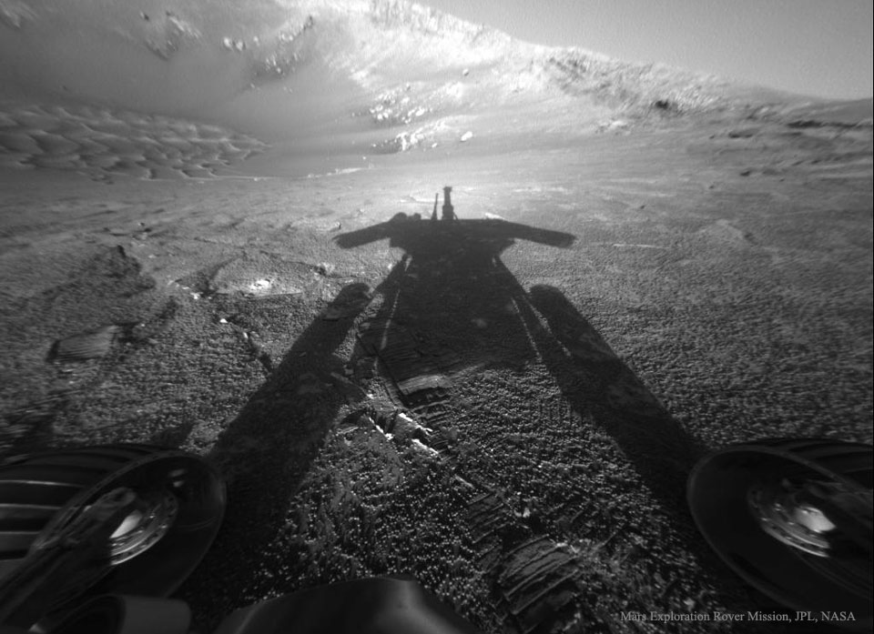 Der Schatten des Marsrovers Opportunity fällt auf den Boden des Kraters Endurance auf dem Mars. Unten ragen seine Räder ins Bild. Um den Schatten der Kamera, die das Bild fotografierte, erkennt man den Oppositionseffekt.