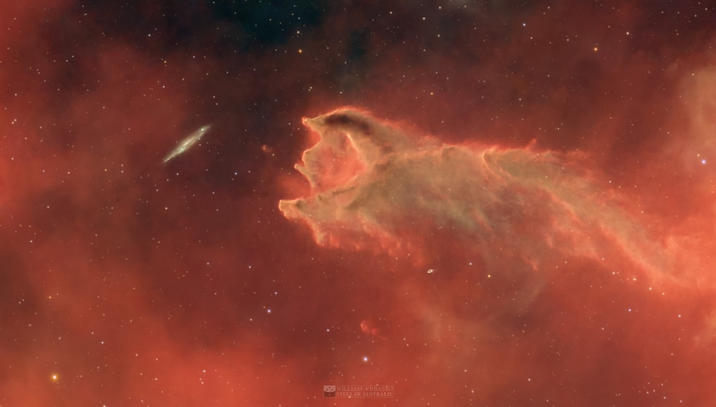 Scheinbar schnappt eine Molekülwolke nach einer Spiralgalaxie. Doch die Wolke ist viel näher. Sie erinnert an eine Hand oder einen gefräßigen Wurm.